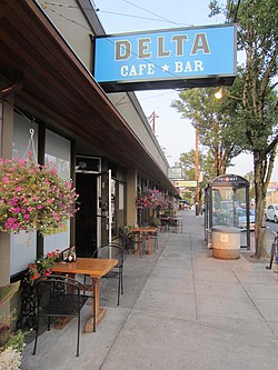 Photograph of a sidewalk and restaurant exterior with outdoor seating and a covered bus stop