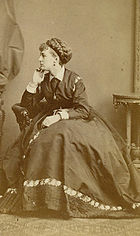 Boulton sitting in profile, wearing an Edwardian dress, with an elaborate wig