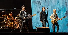 Una fotografia a colori dei membri degli U2 in concerto