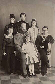 Black-and-white photograph of bald and bearded Alexander III wearing a military uniform and surrounded by his children and wife.