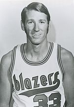 A smiling man wears a Портленд Трейл-Блейзерс jersey.