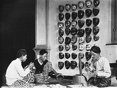 Perajin kayu Jawa membuat topeng tradisional pada era Hindia Belanda.