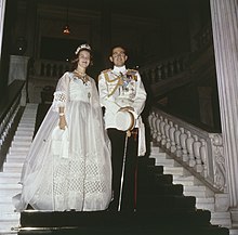 Fotografia colorida mostrando uma mulher em um vestido de noiva e um homem em um uniforme naval em uma escada.