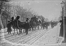 sous la neige s'avance le corbillard tiré par quatre chevaux caparaçonnés de deuil et escorté par des piqueurs