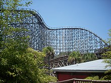The lift hill of the lion track as it ascends 105.4 ft (32.1 m) and turns to the right towards the 91.8 ft (28.0 m) drop. Pieces of track and tree foliage circumnavigate in the foreground.
