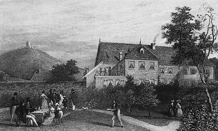 Image en noir et blanc, vaste maison en arrière-fond droit, un mont en arrière-fond gauche, au premier plan une 10e d'hommes et de femmes mangent dans le jardin