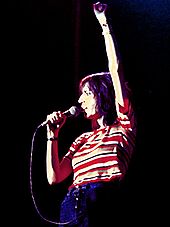 Una foto a colori di Patti Smith in concerto con un microfono