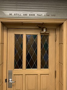 A photo of the door of the chapel in the Fitzsimons Building. Stained glass was installed in the door and also inside the chapel room. Scripture "Be still and know that I am God." Psalm 46:10, is found above the door.