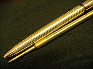 Nib end of gold colored pen body with refill laid into alignment underneath