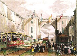 A large crowd standing in a deep railway cutting. On the railway tracks are three elaborately7 decorated carriages and a number of small locomotives.£77