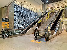 The artwork on the wall behind the escalators leading up to the ground level