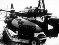‏איש צוות קרקע צובע פצצת 407 קילוגרם בכיתוב "ברכות יום מאי" המתייחס ל-1 במאי (חג הפועלים), ניתן לראות ברקע את מטוס הF-84.‏ 1 במאי 1952.