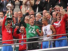 Players celebrating, one of whom is holding aloft a trophy