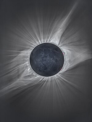 A total solar eclipse, with the earthshine illuminated Moon and the solar corona with its solar prominences (in red) along the lunar limb and coronal streamers streaching out.