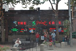 A single story building with a sign that reads "The 5 Point Cafe" and a plaza on a rainy day