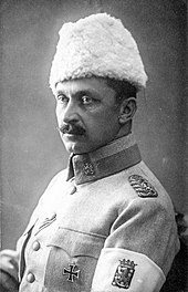 A studio-style picture of General Mannerheim, commander-in-chief of the White Army. He is looking away with his left shoulder turned towards the camera. On his left arm, a white armband shows the coat of arms of Finland.