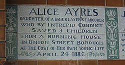 A tablet formed of six standard sized tiles, bordered by green flowers in the style of the Arts and Crafts movement. The tablet reads "Alice Ayres, daughter of a bricklayer's labourer who by intrepid conduct saved 3 children from a burning house in Union Street, Borough, at the cost of her own young life April 24, 1885".