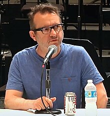 Middle-aged man with glasses and a blue shirt speaking into a microphone