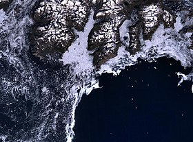 Cap Farvel (au centre de l'image) et la rude côte sud de l'île Egger. La côte (en foncé) est généralement entourée par une mer de glace, rendant la navigation dangereuse.