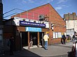 A red-bricked building with a rectangular, blue sign reading "HIGHBURY & ISLINGTON STATION" in white letters all under a blue sky with white clouds