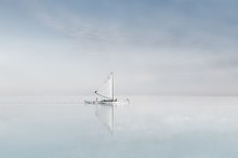 Une athmosphère cotoneuse, composée d'eau et de ciel, tout est calme et plat. Au centre, un petit bateau, avec son reflet estompé, une voile blanche pointée vers le ciel.