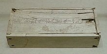 White rectangular box with small cracks and a long line of hieroglyphs along the entire length of the lid, at its centre