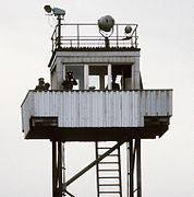 A metal observation tower manned by three GDR guards. Some watchtowers were semi-portable and could be moved to new sectors when needed.[citation needed]