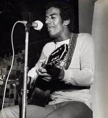 Black and white photo of a man playing guitar and singing into a microphone