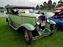 A lime-green 1920s style car with a black foldable top facing forward angled towards the photo's right on grass