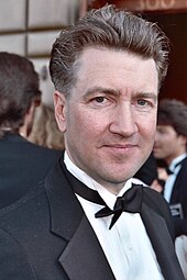 A man in a tuxedo looks directly at the camera, slightly smiling.