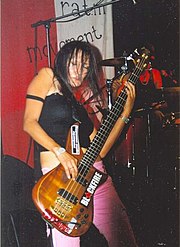 Femme brune, les cheveux devant les yeux, jouant de la guitare.