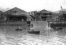 Black-and-white photo of aircraft sheds, facing out onto the sea.
