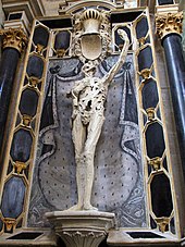 Limestone statue of a putrefied and skinless corpse which looks upwards at his outstretched left hand.