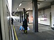 Three people walking on a platform, the one on the left boarding a train, the one in the middle carrying bags, and the one on the right walking through a door