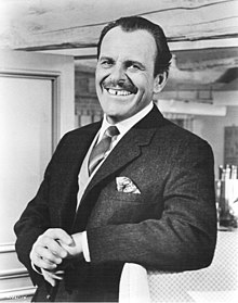 Terry-Thomas from the waist up, in jacket, waistcoat and tie, smiling at the camera