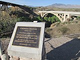 A historical marker for the Ciénega Bridge at the Ciénega Creek Natural Preserve, with the bridge in the background