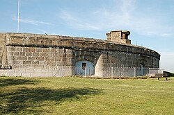 View of the front exterior of the fort showing an arc of casemates, with a structure on the roof