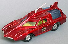 The photograph depicts a scale toy replica of a futuristic car that is deep red in colour and incorporates an angular bonnet and roof.