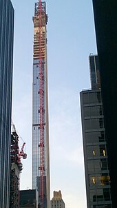A construction crane installing panels on the building's southern facade in July 2019