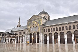 The mosaic-covered facade of a large prayer hall resting on arcades in a marbled courtyard