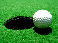 Bola de golfe no green prestes a cair no buraco.