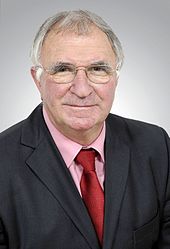A bespectacled, middle-aged man in a suit and tie