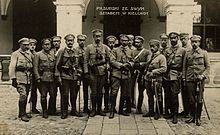 A group of men standing in front of a building. They are dressed in military uniforms.