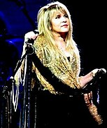 Stevie Nicks is pictured on stage holding a microphone and looking to her left