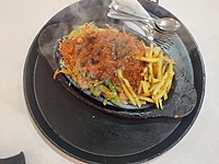 Chicken sizzler is served on high temperature in heavy wood utensils.