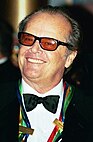 A smiling man wearing tinted sunglasses and a tuxedo