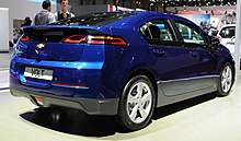 Rear three-quarters view of a blue liftback with short suspension. Photo taken indoors at the Geneva Motor Show in 2013. It is the European-specification Chevrolet Volt.