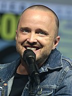 Aaron Paul smiling at San Diego Comic-Con with a microphone in front of him