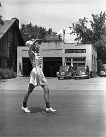 A woman in a marching band uniform, including bobby socks walking down a street