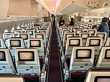 Inside view of an aircraft's Economy Class cabin with television on the back of the seats and overhead lockers on the ceiling